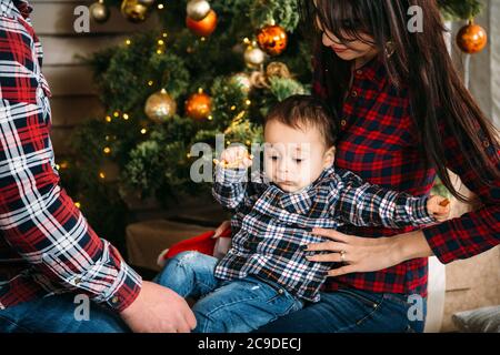 Weihnachten Familienportrait von jungen glücklich lächelnden Eltern spielen mit kleinen Kind in der Nähe des weihnachtsbaums. Winterurlaub Weihnachten und Neujahr Konzept Stockfoto