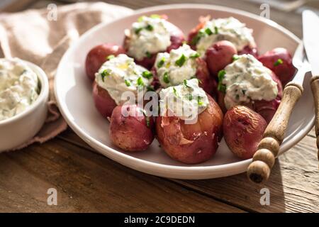 Junge, gekochte Kartoffeln mit Sauerrahm und grüner Zwiebel auf Holzgrund Stockfoto