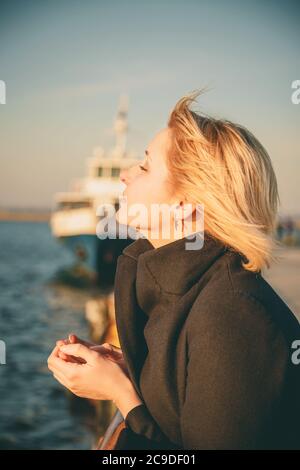 Nahaufnahme der jungen schönen Frau, Mädchen am Pier bei Sonnenuntergang mit geschlossenen Augen genießen Freiheit, glücklich im Freien Porträt Stockfoto