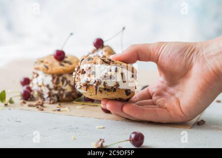 Kirsche-Eis-Sandwiches mit Schokolade Chip Cookies in der Frau Hand Stockfoto