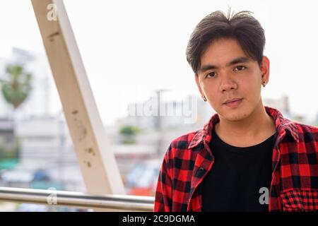 Junge gutaussehende asiatische Hipster Mann auf Fußgängerbrücke in der Stadt Stockfoto