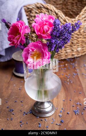 Kleine Vintage Glasvase mit wilden rosa Rosen und lila Lavendel auf Palisander Holztisch Stockfoto