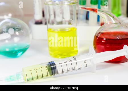 Medizinische Nadel auf dem sterilen Tisch mit flüssigem Impfstoff, gelber Impfstoff gegen Viren. Impfungen und Antibiotika. Chemische Elemente im Labor. Mitarbeiter Stockfoto