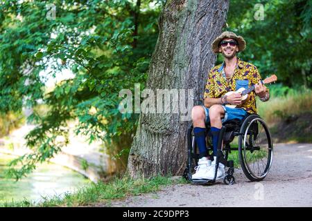 Schöner Mann im Rollstuhl im Freien in einem Park, der Gitarre spielt Stockfoto