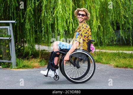 Junger Mann sitzt im Rollstuhl im Freien im Park und lächelt Stockfoto
