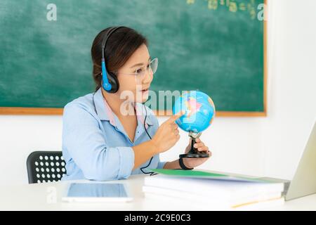 Asiatische Frau Lehrer Geographie über Videokonferenz E-Learning in Laptop mit Tafel im Klassenzimmer unterrichten. Homeschooling und Fernunterricht, auf Stockfoto