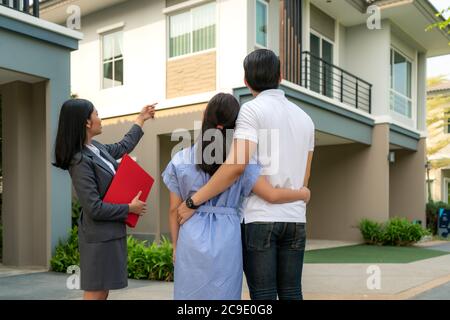 Asian Woman Immobilienmakleragentin, die dem jungen asiatischen Liebespaar, der es sucht und Interesse daran hat, ein Hausprojekt in ihrer Akte ausführlich zeigt. Kaufen Stockfoto