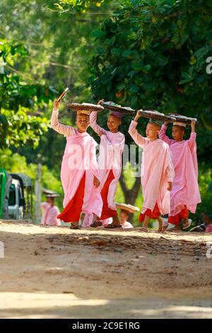 Bagan/Myanmar - 4. Oktober 2019: Eine burmesische Novizenin geht morgens, um Essen zu spenden, indem sie einen Korb auf den Kopf legt. Stockfoto