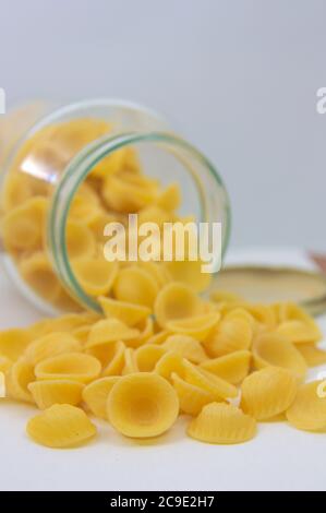Nahaufnahme von einigen Orecchiette, italienische Pasta in der Form von kleinen Ohren, die aus einem Glas mit einem neutralen Hintergrund und Kopierer-Raum ragen Stockfoto