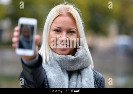 Glückliche junge schöne blonde Frau nimmt Selfie im Park Stockfoto