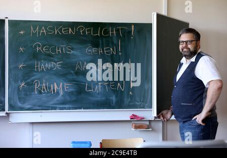 Rostock, Deutschland. Juli 2020. Markus Riemer, Direktor des Innerstädtischen Gymnasiums Rostock ISG, öffnet eine Tafel in einem Klassenzimmer mit der Corona-Anleitung: "Masken sind Pflicht! Gehen Sie nach rechts! Waschen Sie sich die Hände! Räume lüften!“. Mecklenburg-Vorpommern ist das erste Bundesland, das am 03.08.2020 den landesweiten Regelbetrieb der Schulen wieder aufnimmt. Rund 150 Schüler werden nach den Sommerferien in ihren Schulen erwartet. Quelle: Bernd Wüstneck/dpa-Zentralbild/dpa/Alamy Live News Stockfoto