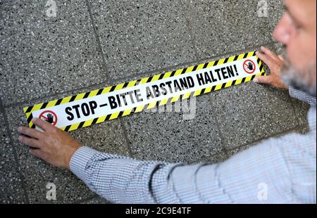 Rostock, Deutschland. Juli 2020. Steffen Stockmann-Schwenn, Hausmeister der CJD Jugenddorf-Christophorusschule Rostock, bringt auf dem Boden einen Aufkleber mit der Aufschrift 'Stop - Bitte halten Sie Abstand! Mecklenburg-Vorpommern ist das erste Bundesland, das am 03.08.2020 den landesweiten Regelbetrieb der Schulen wieder aufnimmt. Rund 150 Schüler werden nach den Sommerferien in ihren Schulen erwartet. Quelle: Bernd Wüstneck/dpa-Zentralbild/dpa/Alamy Live News Stockfoto