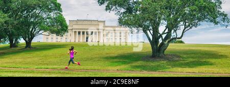 Park Läuferin Frau läuft in Auckland City Banner. Panorama Ernte von Jogging Mädchen auf grünem Gras und Bäumen im Auckland Domain Park mit Memorial Stockfoto