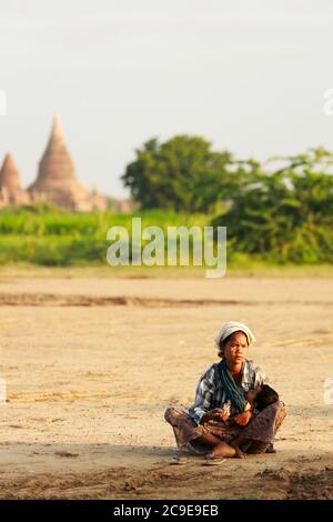 Bagan/Myanmar - 4. Oktober 2019: Eine gebürtige Burmesen trägt ein Baby und bittet um Geld von einem Touristen, der eine alte Pagode in Bagan, Myanmar besucht Stockfoto