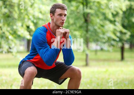 Zugeschnittenes Foto eines jungen attraktiven Mannes, der im Park hockt. Konzept eines aktiven Lebensstils und eines gesunden Lebensstils. Stockfoto
