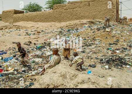 Kinder spielen an einem mit Müll übersäten Ort, während Esel in Timbuktu, Mali, einer Stadt am Rande der Sahara, im Müll nach Nahrung suchen. Stockfoto