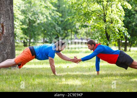 Zwei Männer, die im öffentlichen Park Push-up machten und fünf gaben. Aktives und gesundes Lifestyle-Konzept. Selektiver Fokus. Stockfoto