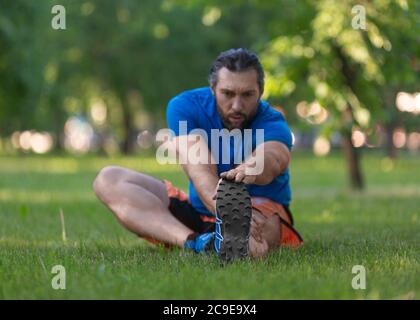 Mann, der sich nach dem Joggen dehnt. Das Konzept eines aktiven Lebensstils und eines gesunden Lebensstils im Alter nach 40 Jahren. Konzentrieren Sie sich auf die Füße. Stockfoto