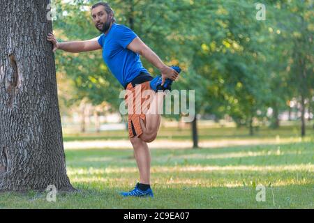 Mann erwärmt Muskeln vor dem Joggen im Freien im Sommer. Das Konzept eines aktiven Lebensstils und eines gesunden Lebensstils im Alter nach 40 Jahren. Stockfoto