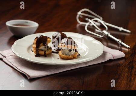 Schokoladencreme und Kakao profiteroles mit heißen geschmolzenen tropfenden Belag. Hintergrund und Rezept Zutaten auf Holztisch Stockfoto