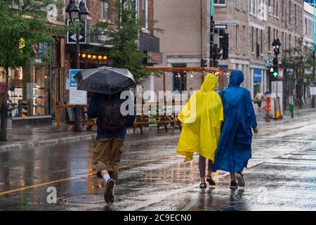 Montreal, CA - 30. Juli 2020: Menschen auf der Mont-Royal Avenue mit Regenschirm und Ponchos bei Regen und Sturm Stockfoto