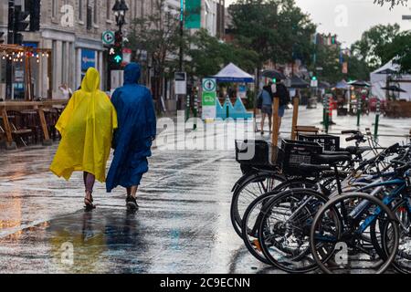 Montreal, CA - 30. Juli 2020: Menschen auf der Mont-Royal Avenue tragen Ponchos bei Regen und Sturm Stockfoto