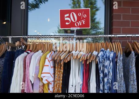 Ermäßigte Mode Kleider, Pullover und Jeans, die an einem Kleiderständer vor einem Einzelhandelsgeschäft hängen. Verkauf auf dem Bürgersteig im Sommer. Stockfoto