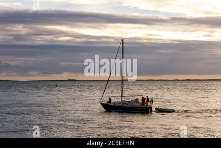 Anglesey, Wales, UK 08/26/2012: Ein kleines Boot mit drei Passagieren in ihm segelt vor der Küste von Wales bei Sonnenuntergang. Ein aufblasbares Boot ist an Th gebunden Stockfoto