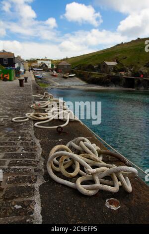 Nahaufnahme von verwickelten Festmacherseilen, die an Metallringen auf einem Steindock gebunden sind. Diese Schiffsseile werden verwendet, um Boote an den Kai in diesem kleinen Fischchen zu binden Stockfoto