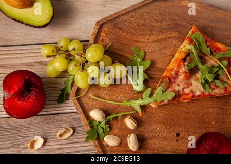 Nahaufnahme Bild von frischen Stein gebacken vegetarische Tomaten und Käse Pizza mit Auberginen Belag. Es wird neben Trauben, Pistazien und Rucola le serviert Stockfoto