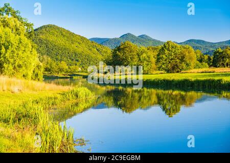 Kroatien, schöner Fluss Gacka fließt zwischen den grünen Wiesen Felder in Lika Region Stockfoto