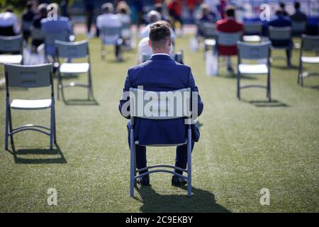 Menschen sitzen auf Stühlen auseinander, um die soziale Distanz während des Covid-19 Ausbruchs bei einem Outdoor-Event auf dem Rasen eines Stadions aufrecht zu erhalten. Stockfoto