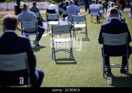 People sit on chairs apart one from another to maintain the social distance during the Covid-19 outbreak at an outdoor event on the turf of a stadium. Stockfoto