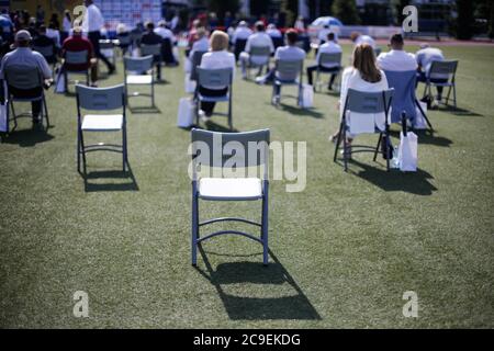 People sit on chairs apart one from another to maintain the social distance during the Covid-19 outbreak at an outdoor event on the turf of a stadium. Stockfoto