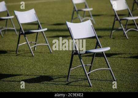 Stühle auseinander, um die soziale Distanz während der Covid-19 Ausbruch bei einem Outdoor-Event auf dem Rasen eines Stadions zu halten. Stockfoto