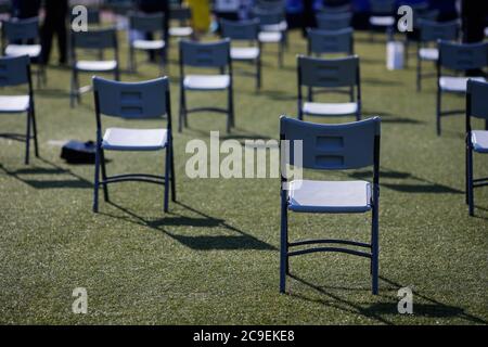 Stühle auseinander, um die soziale Distanz während der Covid-19 Ausbruch bei einem Outdoor-Event auf dem Rasen eines Stadions zu halten. Stockfoto