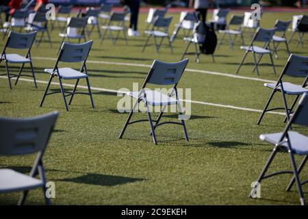 Chairs apart one from another to maintain the social distance during the Covid-19 outbreak at an outdoor event on the turf of a stadium. Stockfoto