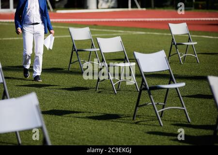 Stühle auseinander, um die soziale Distanz während der Covid-19 Ausbruch bei einem Outdoor-Event auf dem Rasen eines Stadions zu halten. Stockfoto