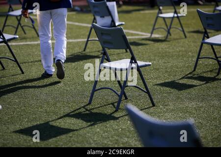 Chairs apart one from another to maintain the social distance during the Covid-19 outbreak at an outdoor event on the turf of a stadium. Stockfoto