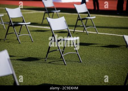 Chairs apart one from another to maintain the social distance during the Covid-19 outbreak at an outdoor event on the turf of a stadium. Stockfoto