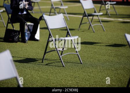 Stühle auseinander, um die soziale Distanz während der Covid-19 Ausbruch bei einem Outdoor-Event auf dem Rasen eines Stadions zu halten. Stockfoto