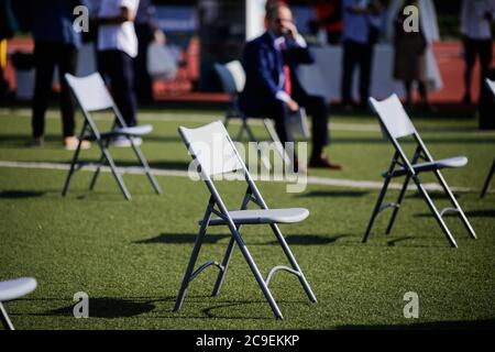 Stühle auseinander, um die soziale Distanz während der Covid-19 Ausbruch bei einem Outdoor-Event auf dem Rasen eines Stadions zu halten. Stockfoto