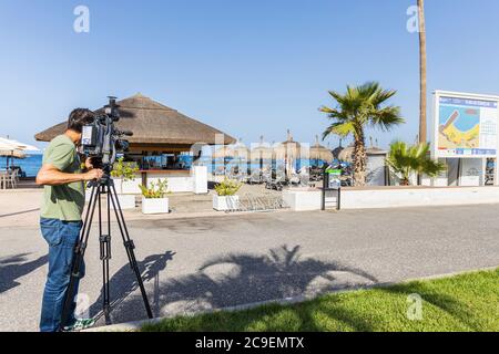 Costa Adeje, Teneriffa, Kanarische Inseln, Spanien. 24. Juli 2020. TV-Kameramann Filme auf Playa Fanabe Strand für einen Bericht über die Insel begrüßt zurück Touristen Stockfoto