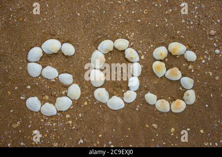 Inschrift auf dem Sand von Muscheln - sos, Camping, Wandern Gefahr Stockfoto