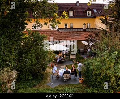 Gäste sitzen an gedeckten Tischen unter Sonnenschirmen im Garten des Hotel Mühle in Binzen, Markgräflerland, Baden-Württemberg, Deutschland. Der idyllische Garten bietet Platz für mehrere Sitzgruppen; eine diskrete Verwandlung hin zu mehr italienischer dolce vita ist für Hotel Mühle und Restaurant La Cucina geplant. Stockfoto