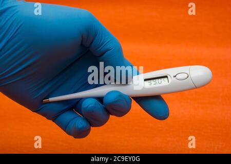 Hand in einem medizinischen Handschuh hält ein elektronisches Thermometer - Temperaturmessung, Coronavirus, covid19 Stockfoto