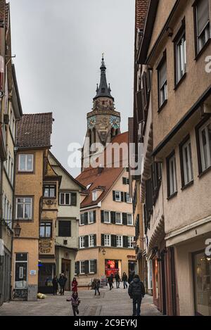 Menschen in einer mittelalterlichen engen Gasse mit St. George Kirche (Stiftskirche St. Georg) Der Glockenturm ragt aus den Fachwerkhäusern heraus Tübingen Stockfoto