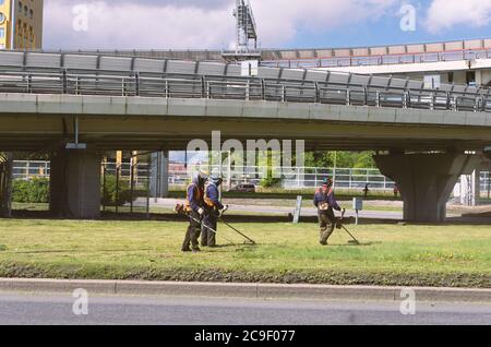 Sankt Petersburg, Russland - 26. Juli 2020: Drei Arbeiter in Overalls mähen das Gras auf dem Rasen mit Trimmern Stockfoto