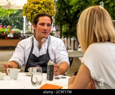 Chef Marc Homberger vom Hotel Florhof in Zürich, Schweiz – erbaut 1763 als Seidenweberei-Familienanwesen für die Oeri-Lavaters, seit 1907 ein Hotel – spricht während eines Interviews mit der Journalistin Angela Berg auf der Gartenterrasse, mit einem Diktiergerät und einem Notizblock auf dem Tisch. Mit 14 Punkten von Gault Millau bewertet, ist der Chef für seine kreative saisonale Küche bekannt und hält japanische Lagenwachteln in seinem Hausgarten, deren Eier er in seinen Gerichten verwendet. Stockfoto