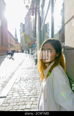 Glückliche junge schöne asiatische touristische Frau lehnt an der Wand in den Straßen von Schweden Stockfoto